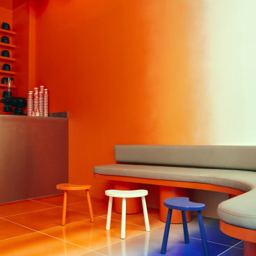 Colorful interior design of Café Nuances featuring vibrant orange walls, unique stools, and a gradient floor, highlighting a psychedelic theme.