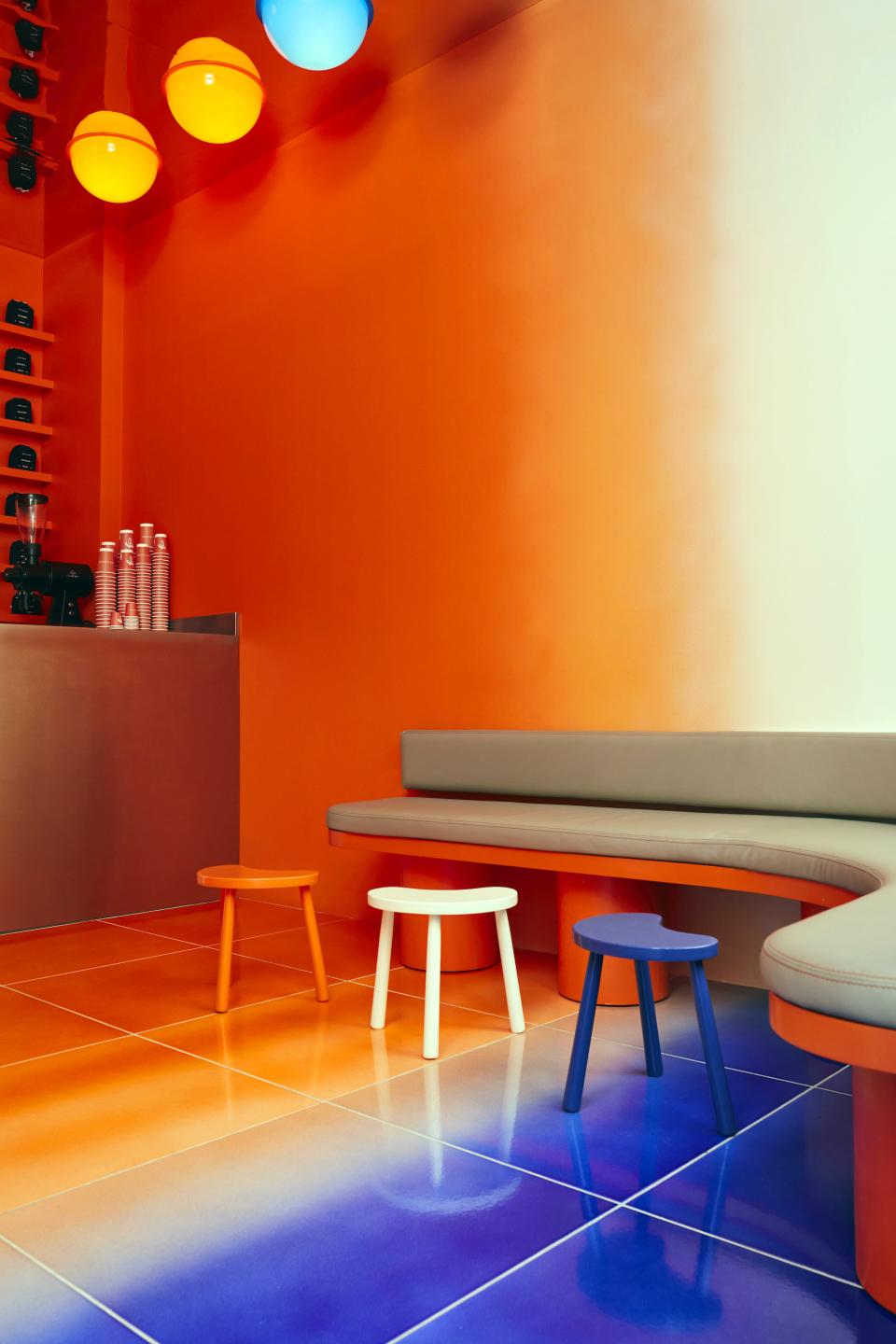 Colorful interior design of Café Nuances featuring vibrant orange walls, unique stools, and a gradient floor, highlighting a psychedelic theme.