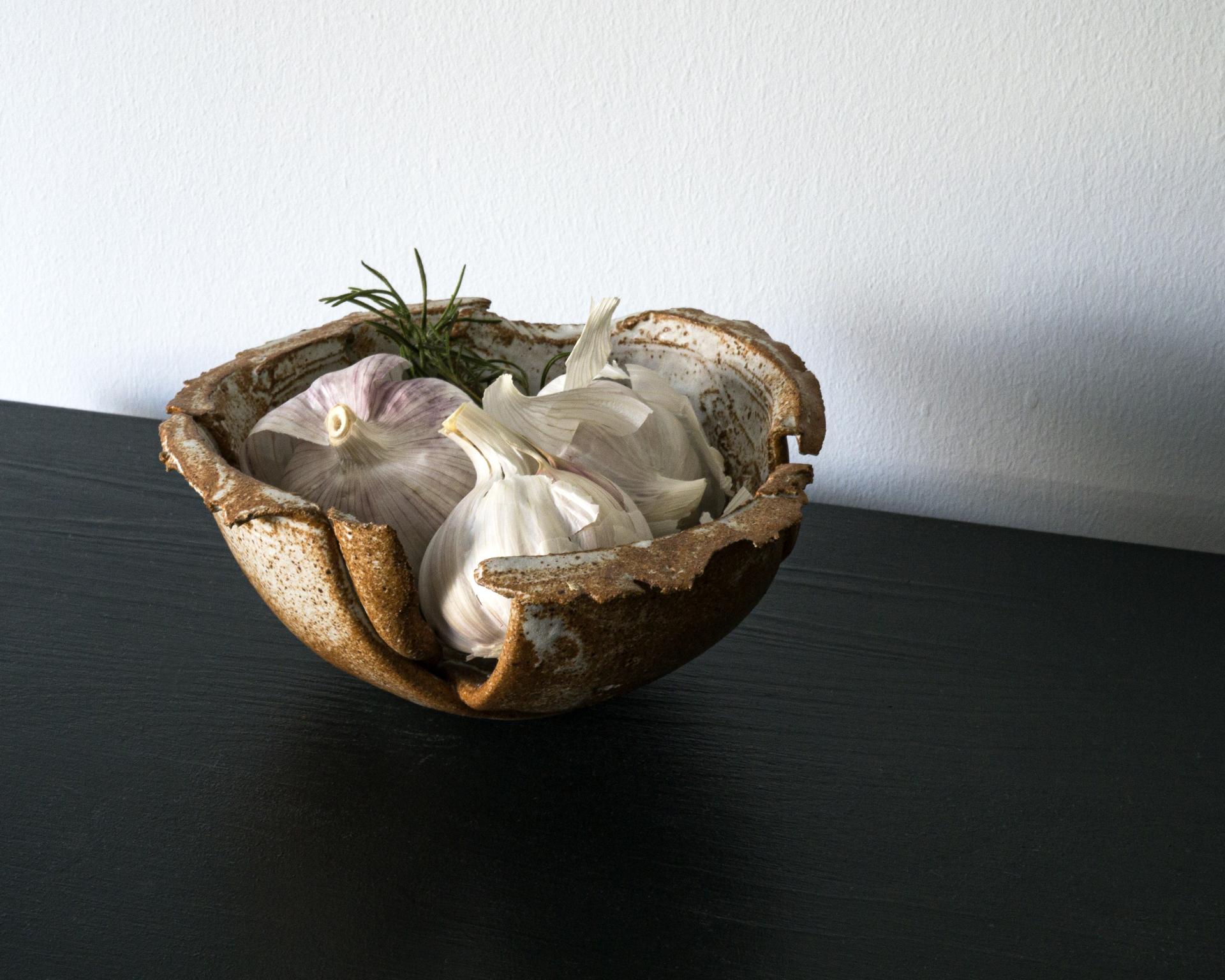 Handcrafted ceramic bowl showcasing fresh garlic and rosemary, reflecting Ewan Crallan's playful, purposeful design style.
