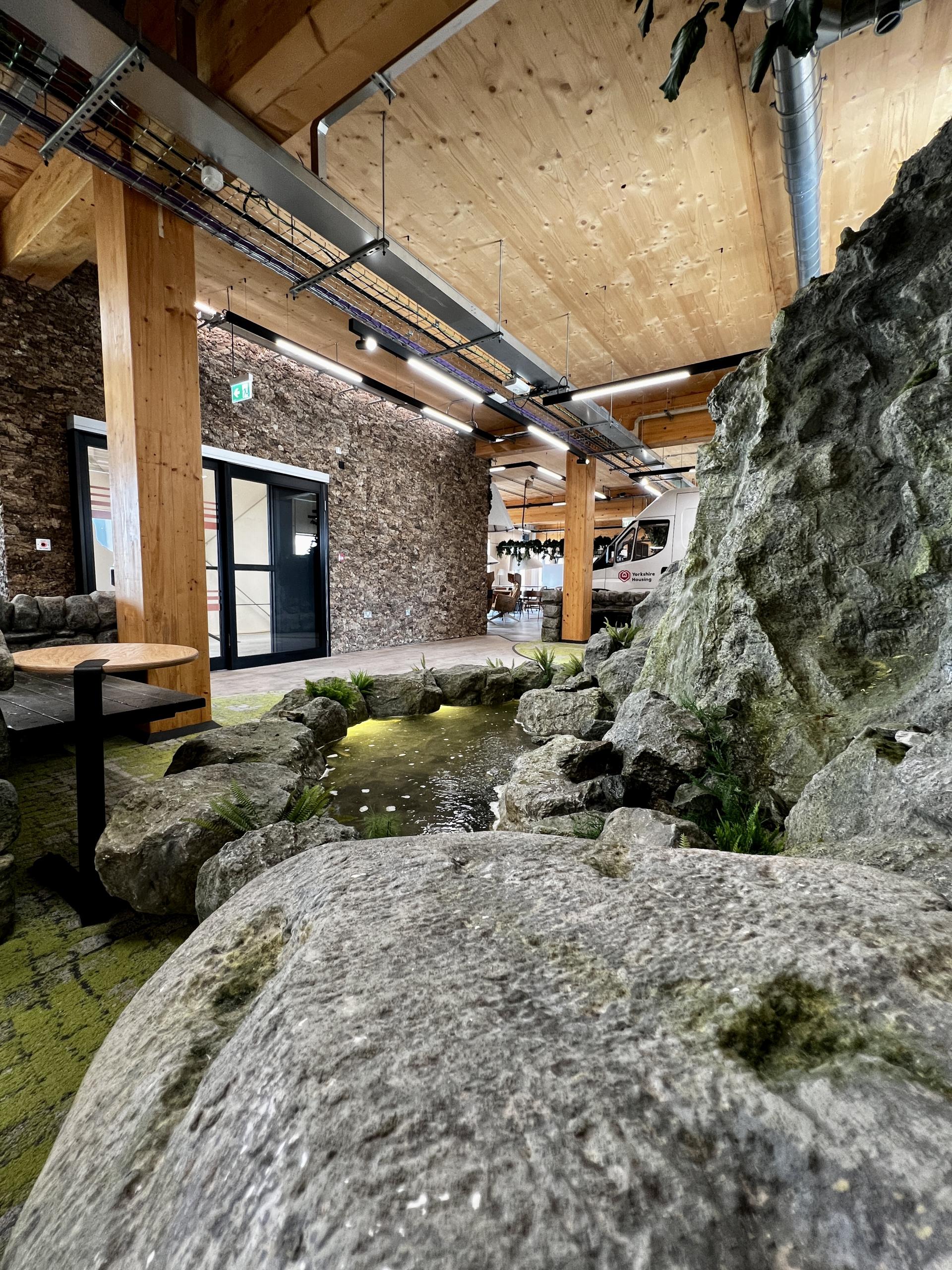 Interior view of Leeds' first net zero carbon workspace featuring a decorative stone pond and lush greenery.