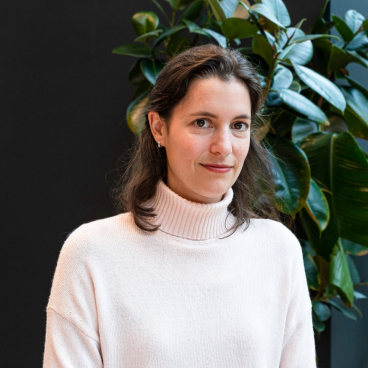 Senior sustainability specialist Astrid Hugo poses in front of green plants, advocating for regenerative design and climate action.