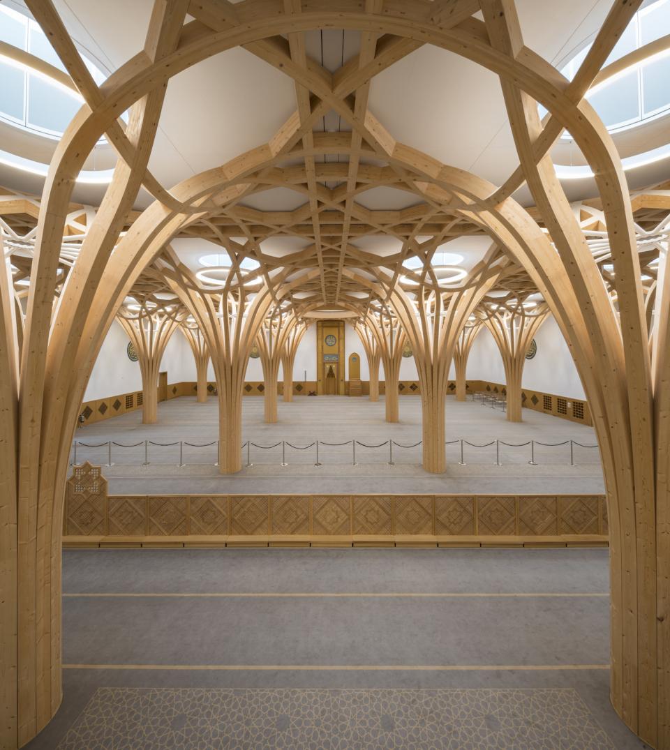 Stunning interior of Cambridge Central Mosque featuring wooden arches and sustainable design elements in a spacious prayer hall.
