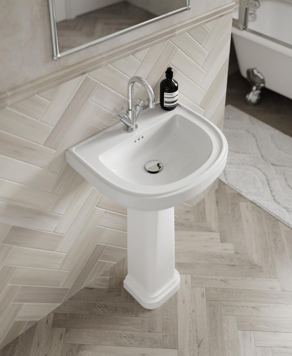 Elegant white pedestal sink against herringbone tiled wall, reflecting classic bathroom design inspired by vintage aesthetics.