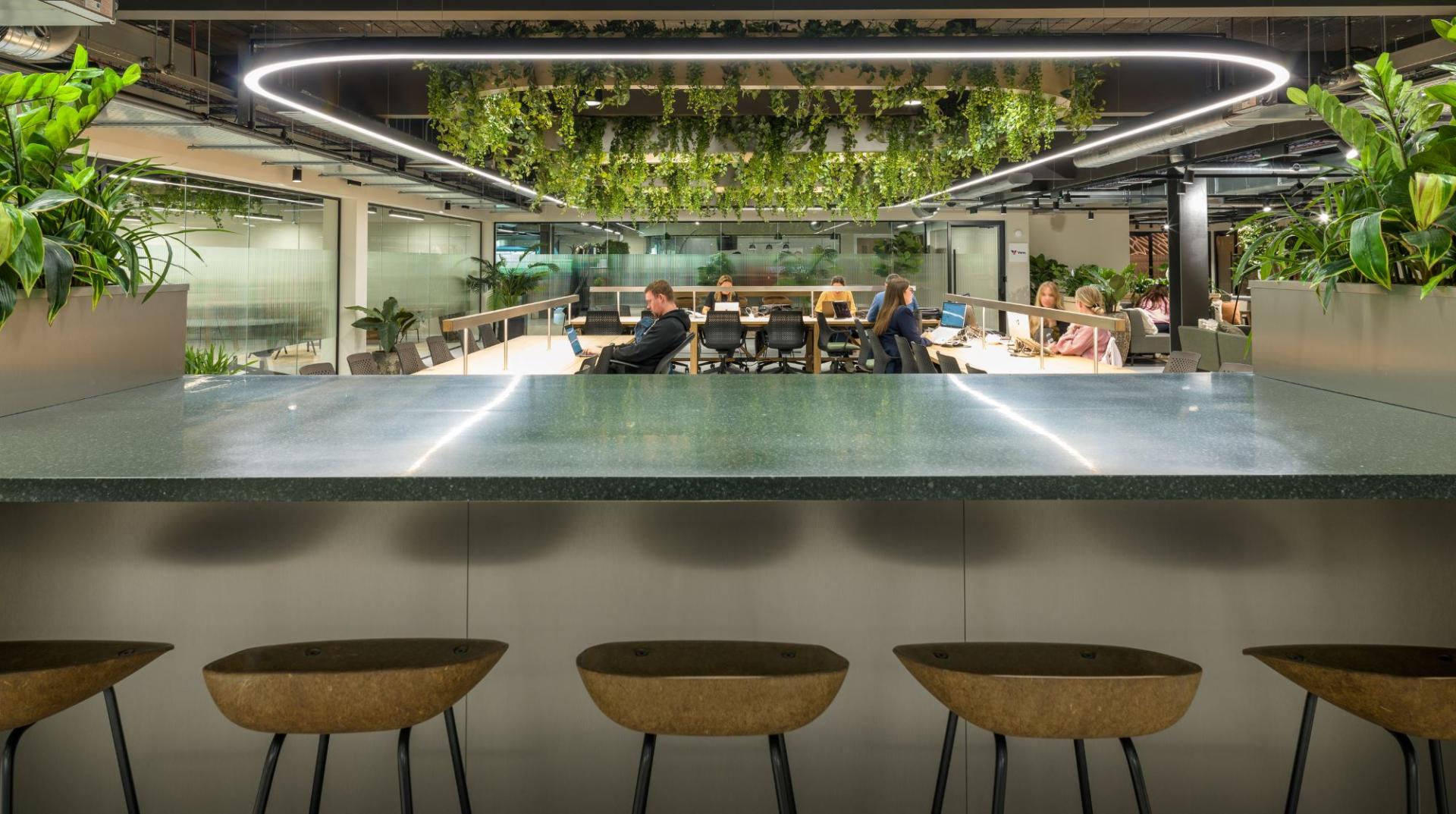 Modern workspace featuring a green-themed design with plants, collaborative areas, and people working at Alderley Park.