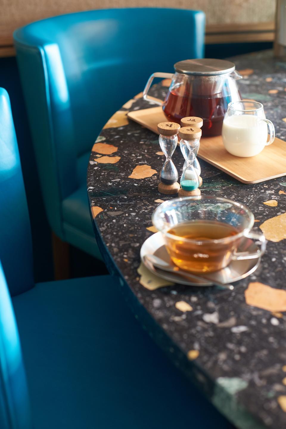 Stylish art deco table setting with tea, hourglasses, and a vibrant blue chair at Teatulia's tea shop.