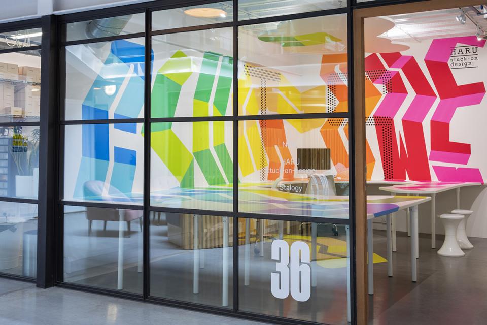 Vibrant interior design featuring HARU Stuck-on Design on glass walls, showcasing colorful geometric patterns and modern workspace elements.