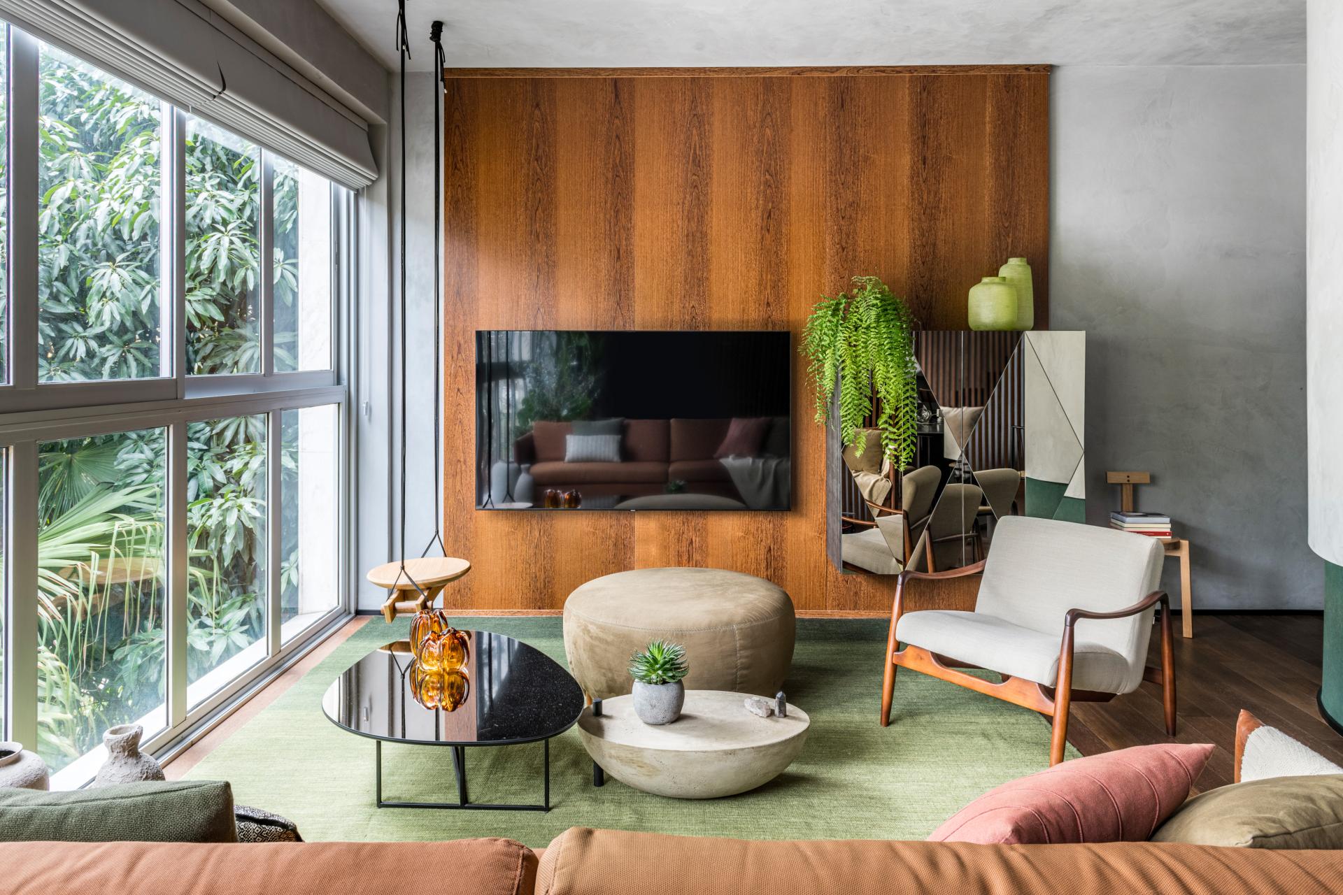 Modern living room design featuring natural elements, vibrant colors, and a view of lush greenery in São Paulo.