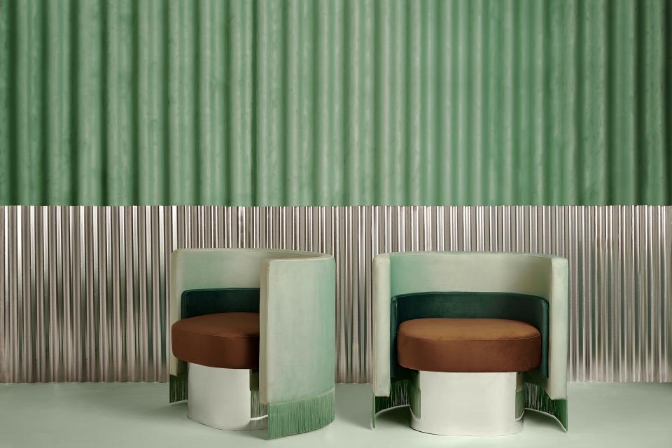 Vintage-inspired lounge chairs by Masquespacio, featuring green upholstery and unique metallic bases, against a textured wall backdrop.