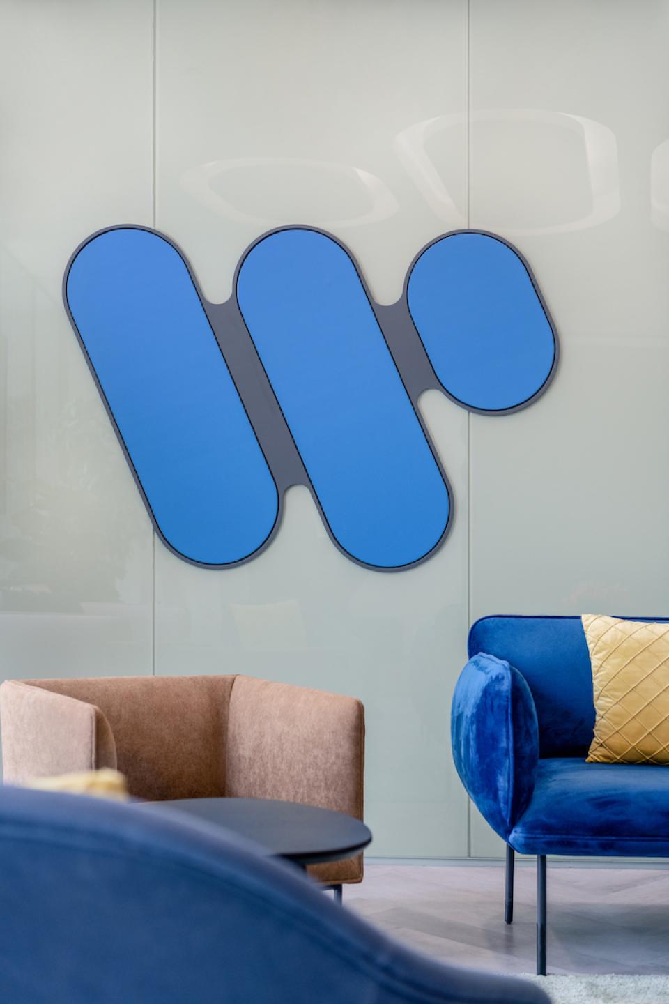 Colorful Warner Music logo displayed on a modern office wall, surrounded by stylish seating in an innovative workplace design.