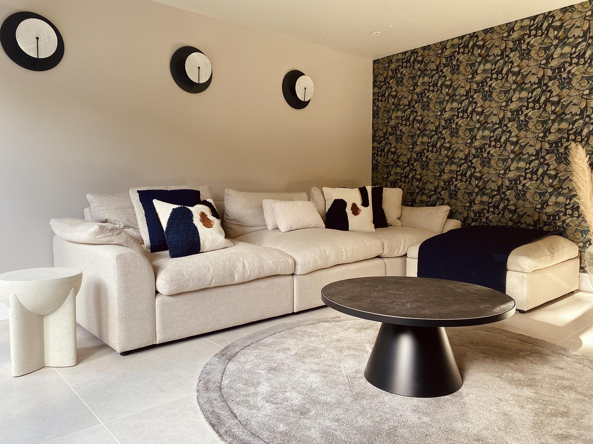 Stylish living room featuring a comfortable beige sofa, decorative pillows, a modern coffee table, and elegant wallpaper.