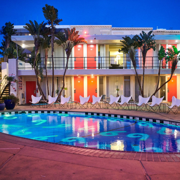 Phoenix Hotel’s vibrant courtyard features a beautifully lit pool surrounded by tropical plants and contemporary lounge chairs.