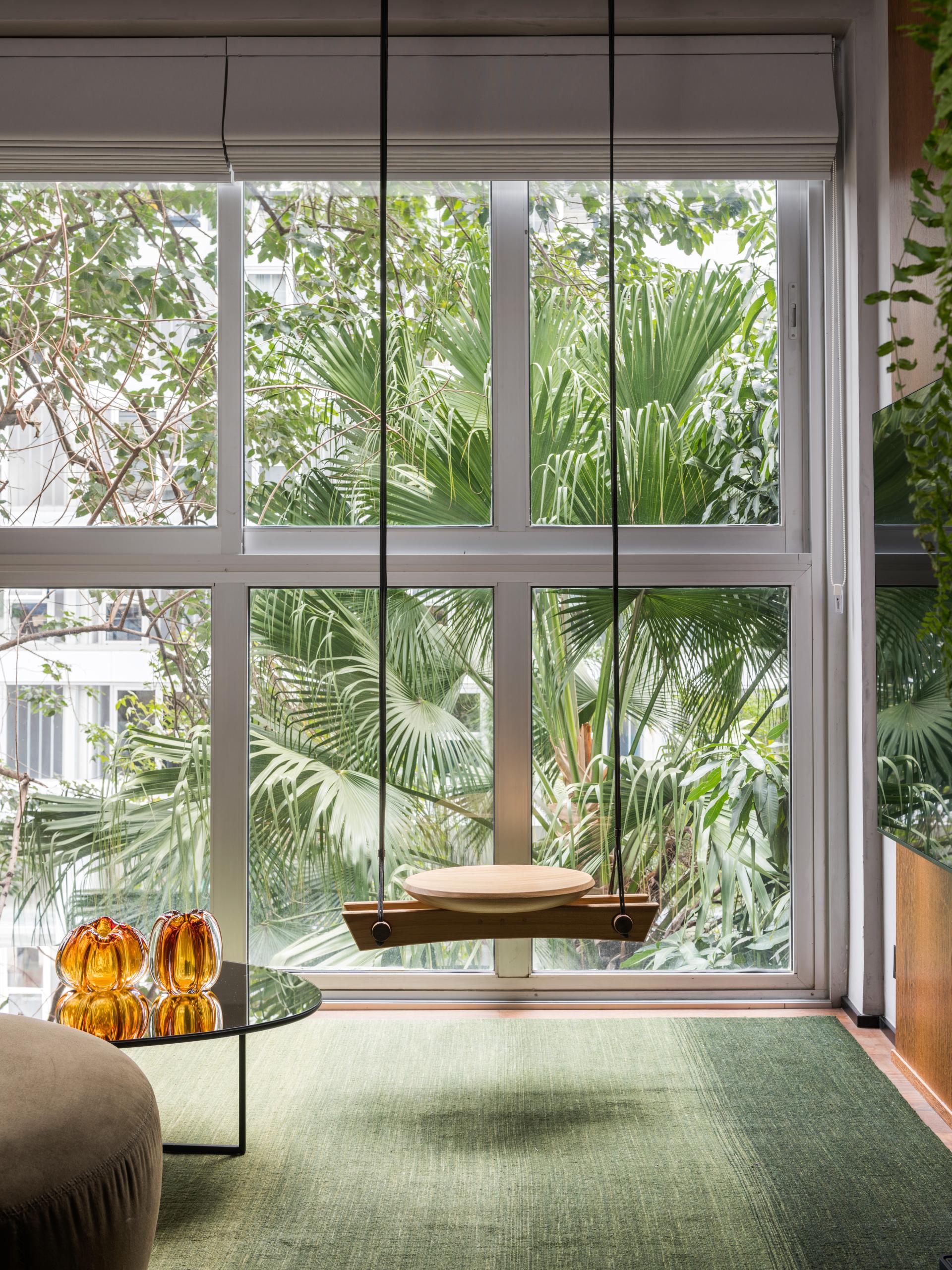 Modern interior featuring a wooden swing, glass coffee table, and vibrant greenery, highlighting the harmony between architecture and nature.