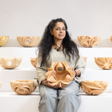 Halima Cassell poses with a sculptural ceramic bowl, surrounded by her intricate handmade ceramic pieces on display.