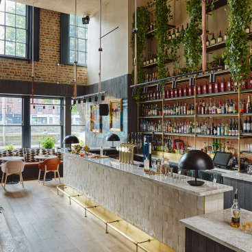 Stylish bar area at Zanzibar Locke aparthotel, featuring retro decor, greenery, and an extensive selection of drinks.