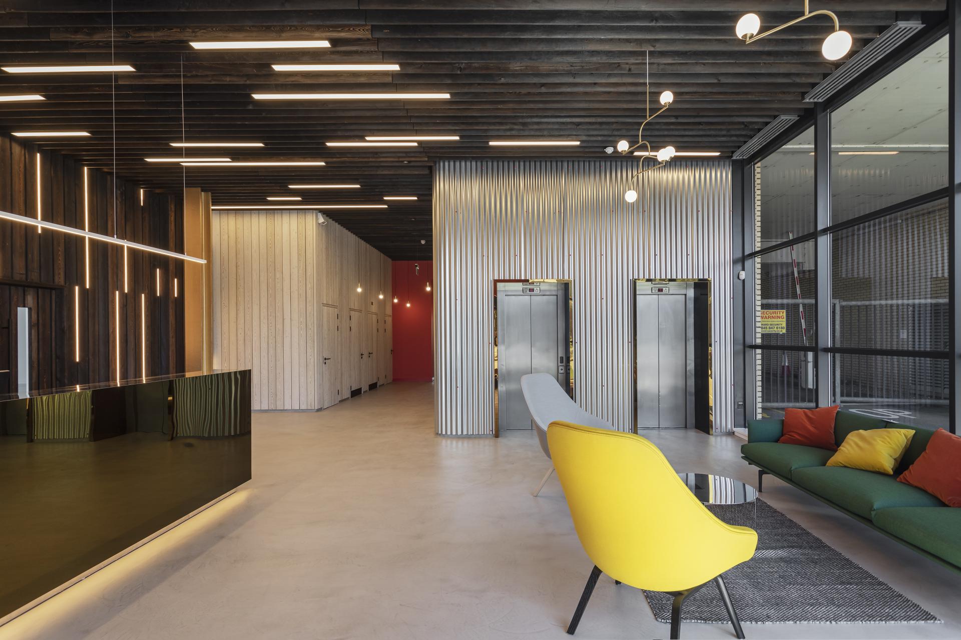 Modern office lobby featuring sleek design elements, vibrant seating, and stylish lighting fixtures in a renovated building.