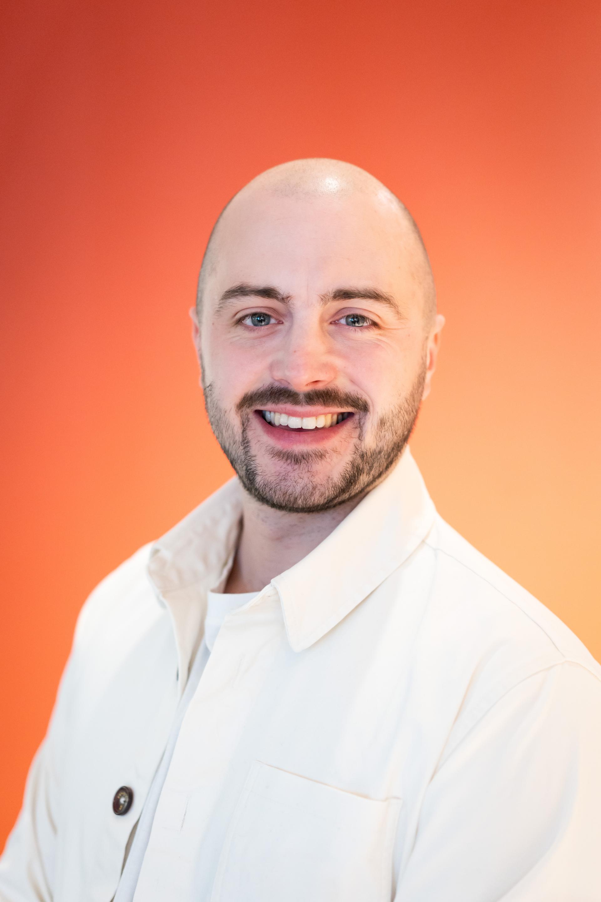 Smiling man in a white jacket against an orange background, representing modern workplace flexibility and leadership.