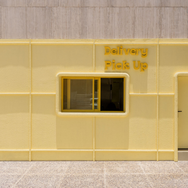 Bright yellow exterior of the Novu Waffle house featuring a "Delivery Pick Up" window and modern design elements.