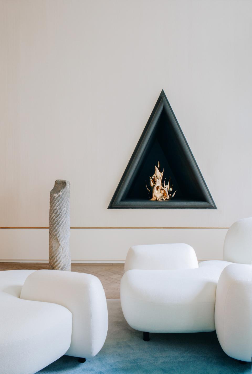 Modern furniture by Mathieu Lehanneur featuring sculptural white seating and an artistic triangular fireplace in a minimalist setting.