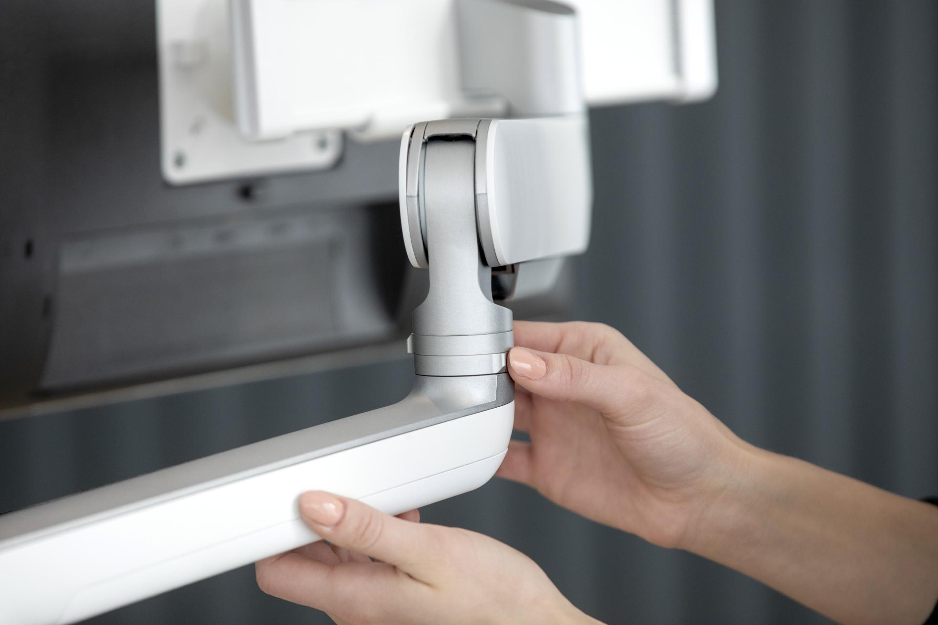 Hands adjusting the flexible connection of a Fellowes Rising™ monitor arm, showcasing its adaptable design for workplace inclusivity.
