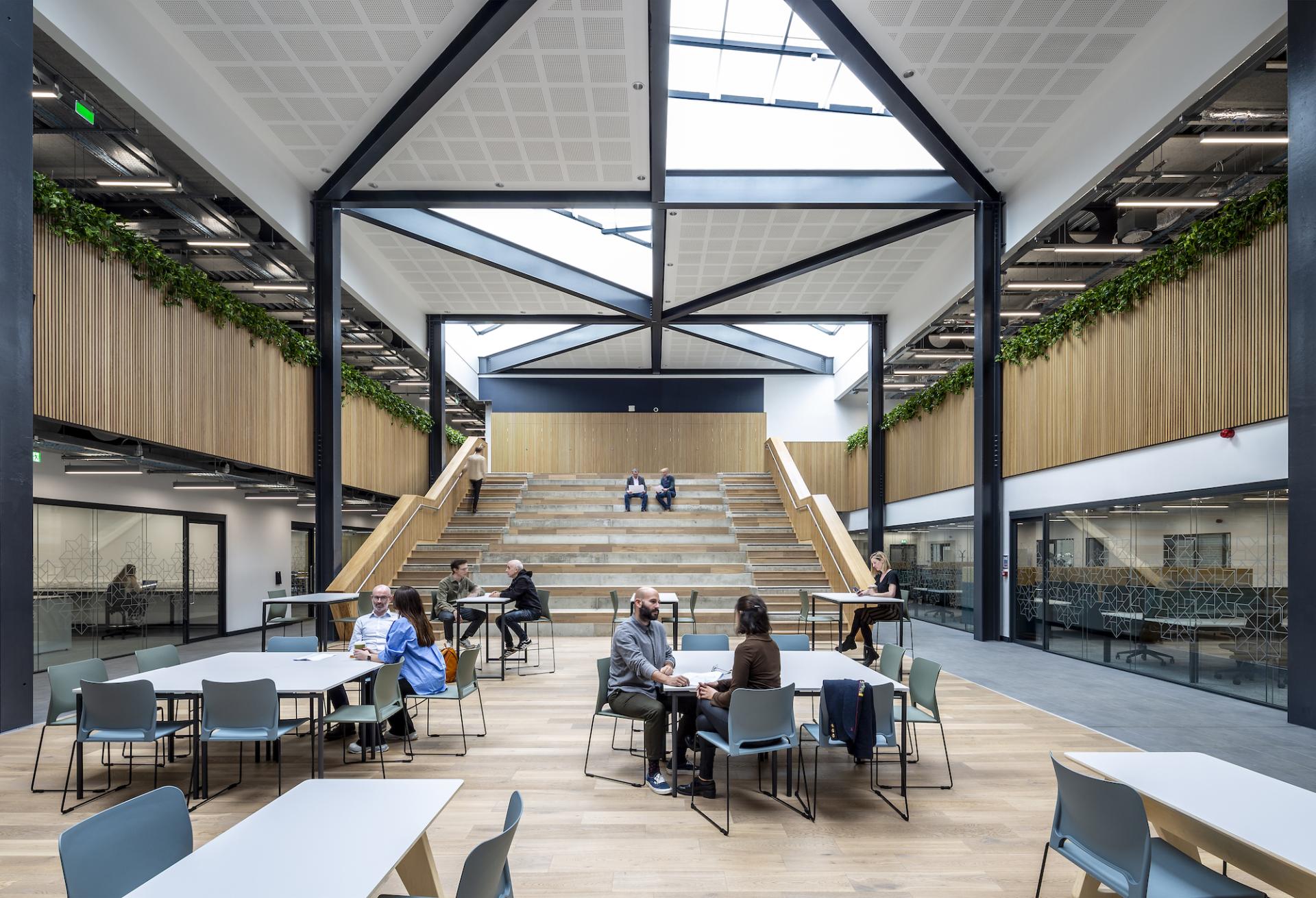 Modern workspace design featuring open seating, collaborative areas, and a striking staircase in a well-lit architectural setting.