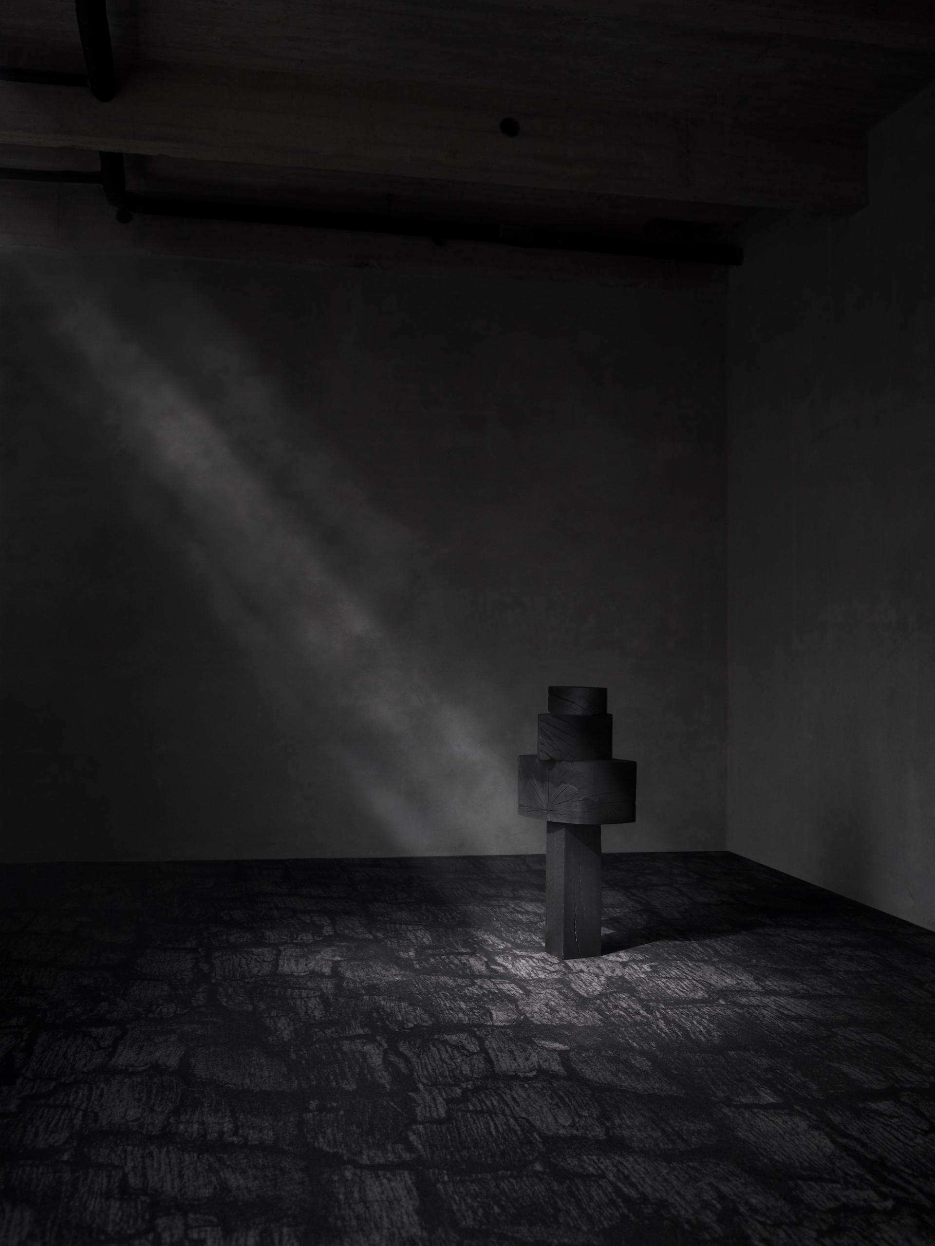 Dark, minimalist interior featuring EGE Carpets' Industrial Landscape design with a sculptural element illuminated by light.