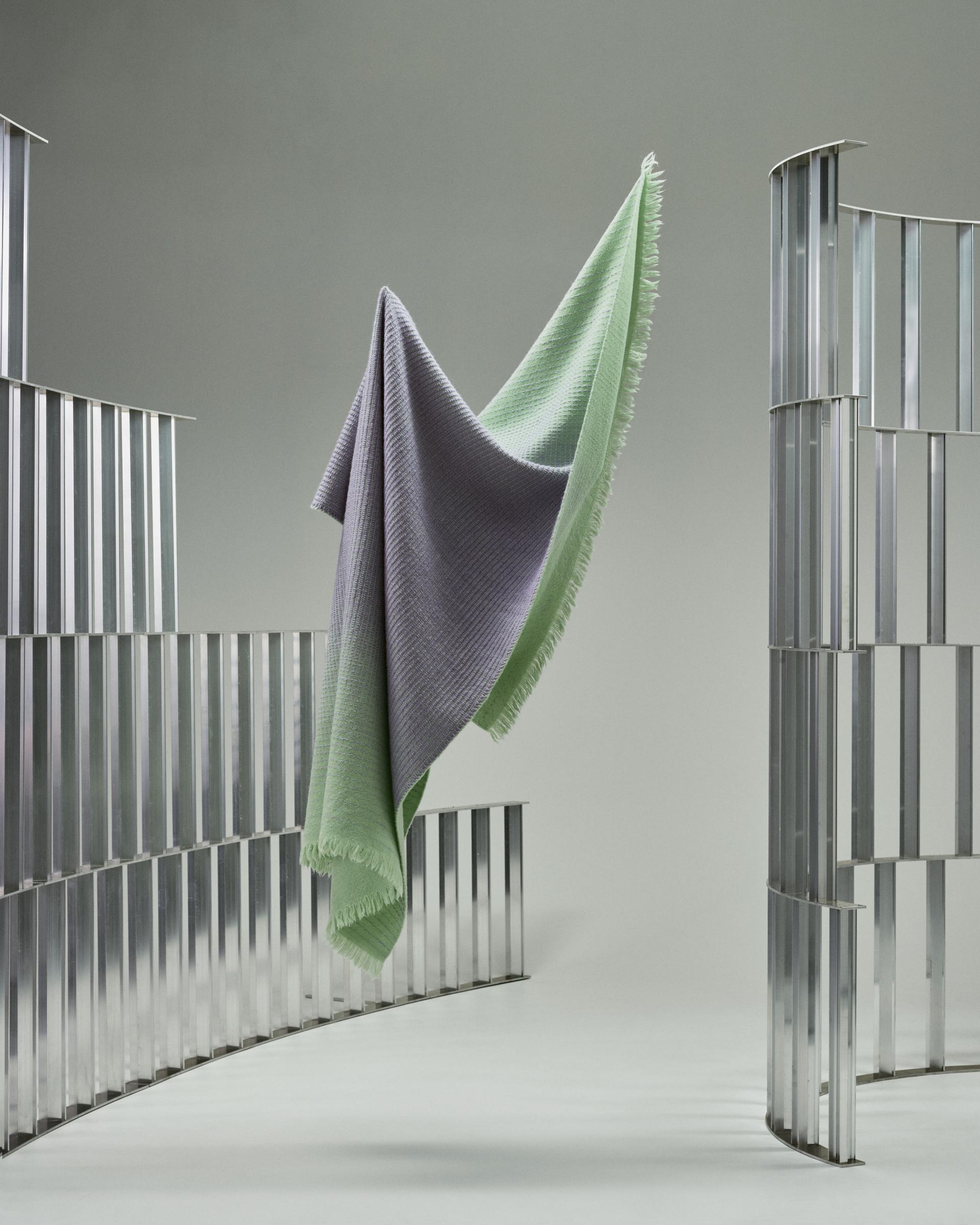 A suspended green and purple textile drapes gracefully between sleek metal sculptures, showcasing circular design at Norwegian Presence 2023.