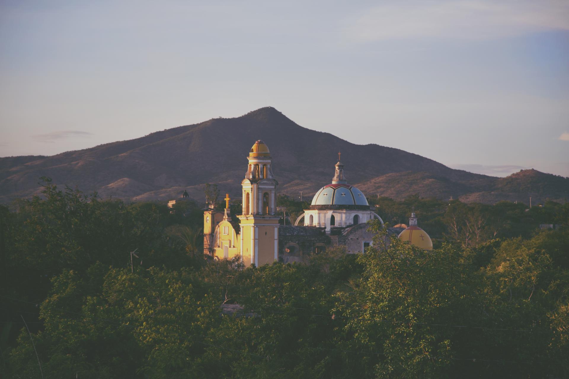 Colorful church architecture nestled among trees and mountains, representing cultural heritage and natural beauty in Totomoxtle.