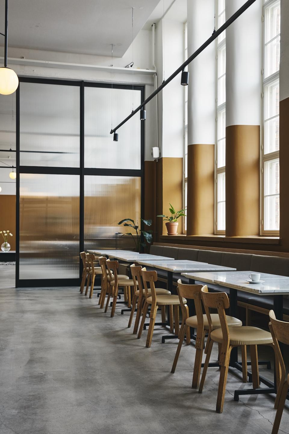 Modern café interior in a refurbished bread factory featuring wooden chairs, marble tables, and large windows.