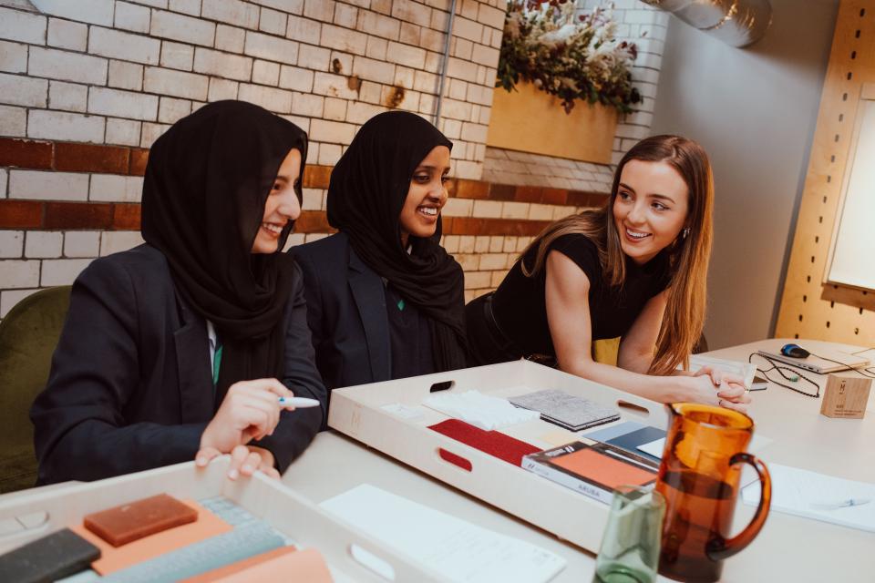 Three interior design students engage in creative collaboration while discussing materials and ideas during a workshop.