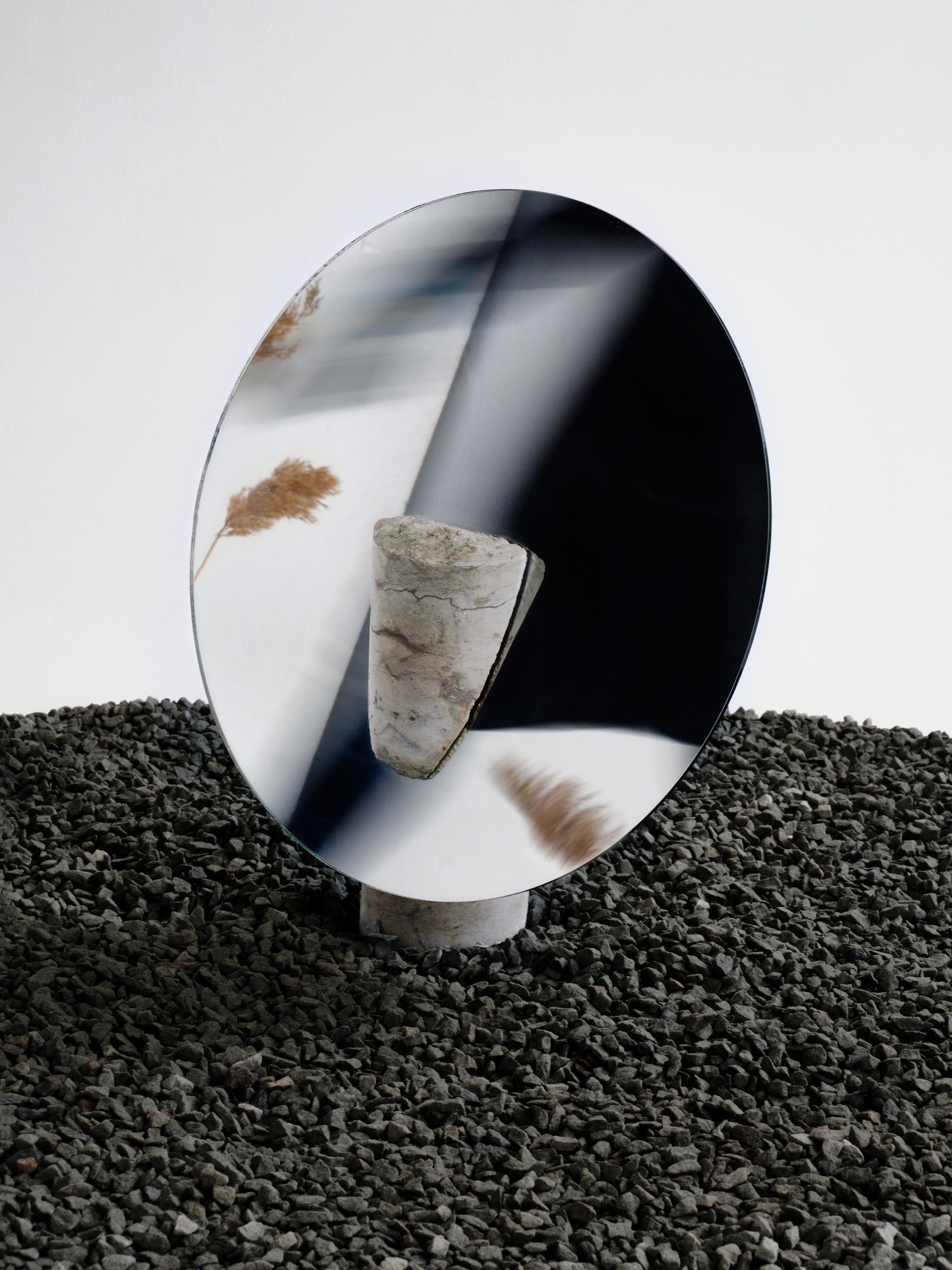 Abstract sculpture combining reflective materials and natural elements on textured gravel, highlighting Baltic innovation in design.