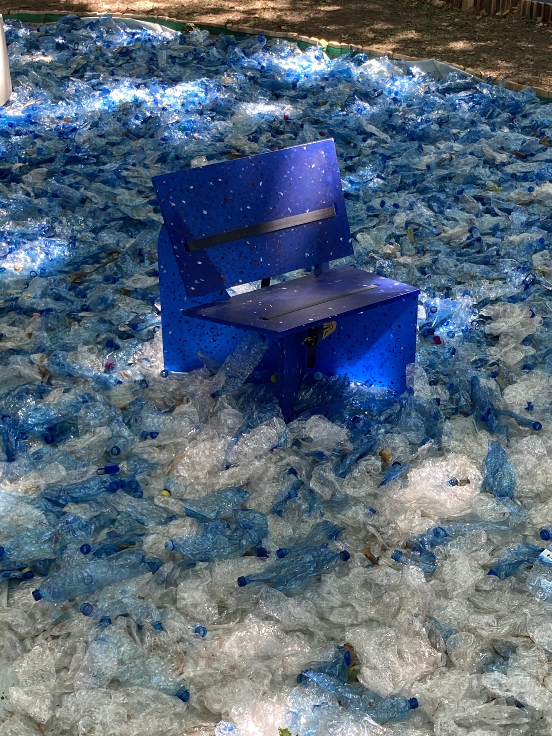Blue recycled plastic chair placed on a bed of crushed plastic bottles, highlighting sustainability themes at the London Design Festival.
