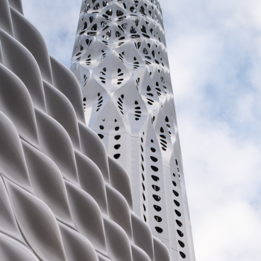 Tower of Light featuring intricate lattice design, part of Manchester's zero-carbon initiative, against a cloudy sky.