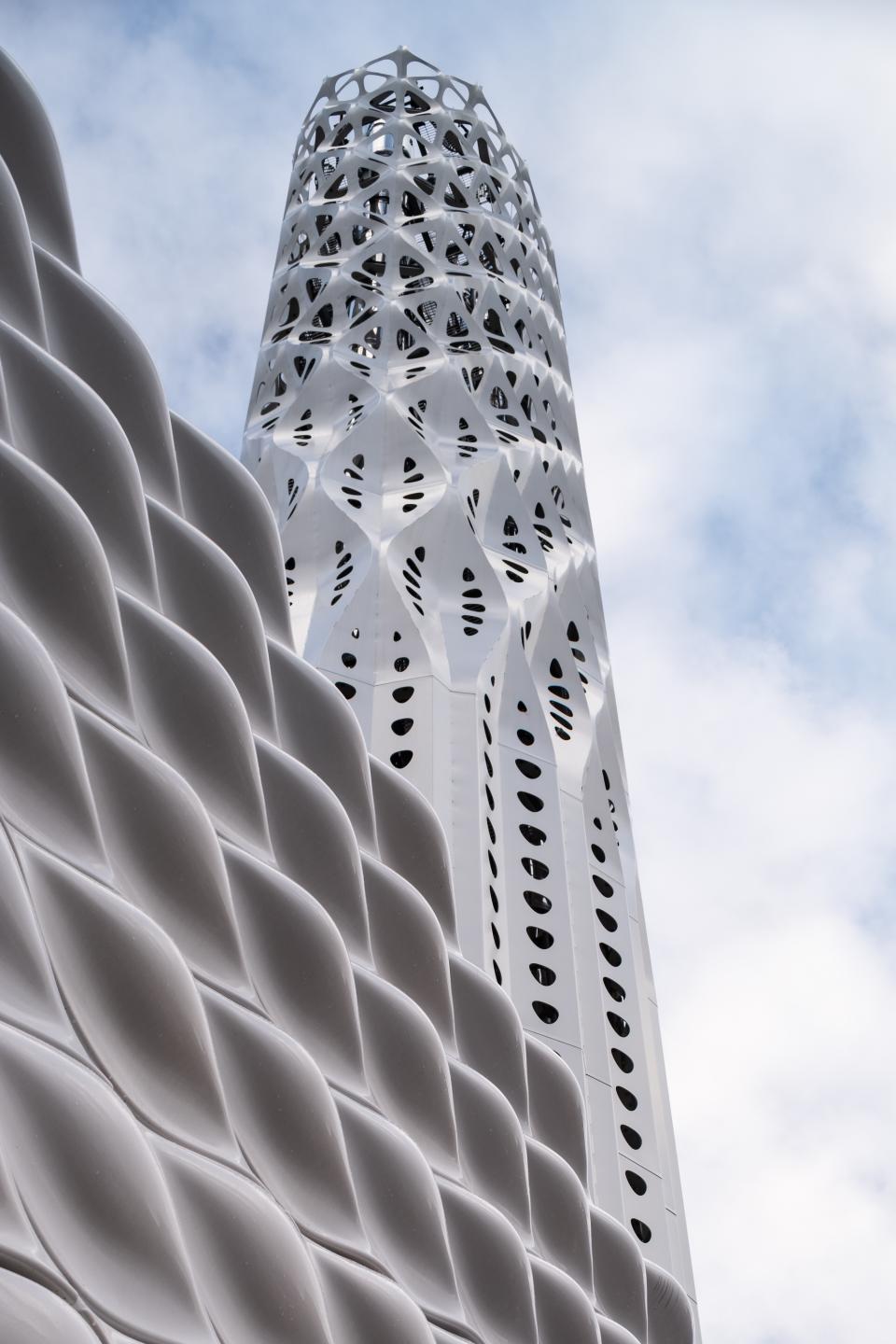Tower of Light featuring intricate lattice design, part of Manchester's zero-carbon initiative, against a cloudy sky.