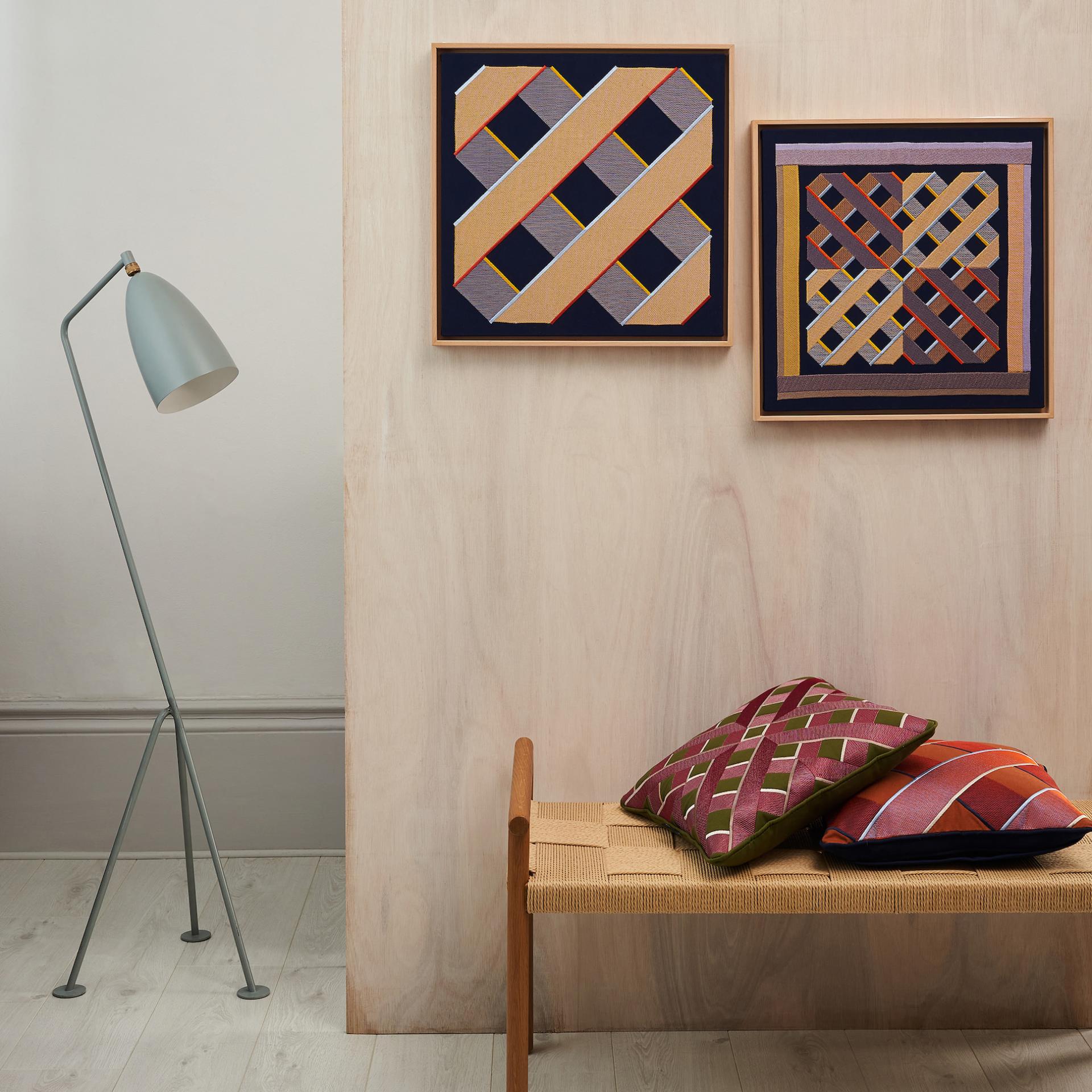 Digital embroidery artworks displayed on a wall, with decorative cushions on a wooden bench and a stylish lamp.