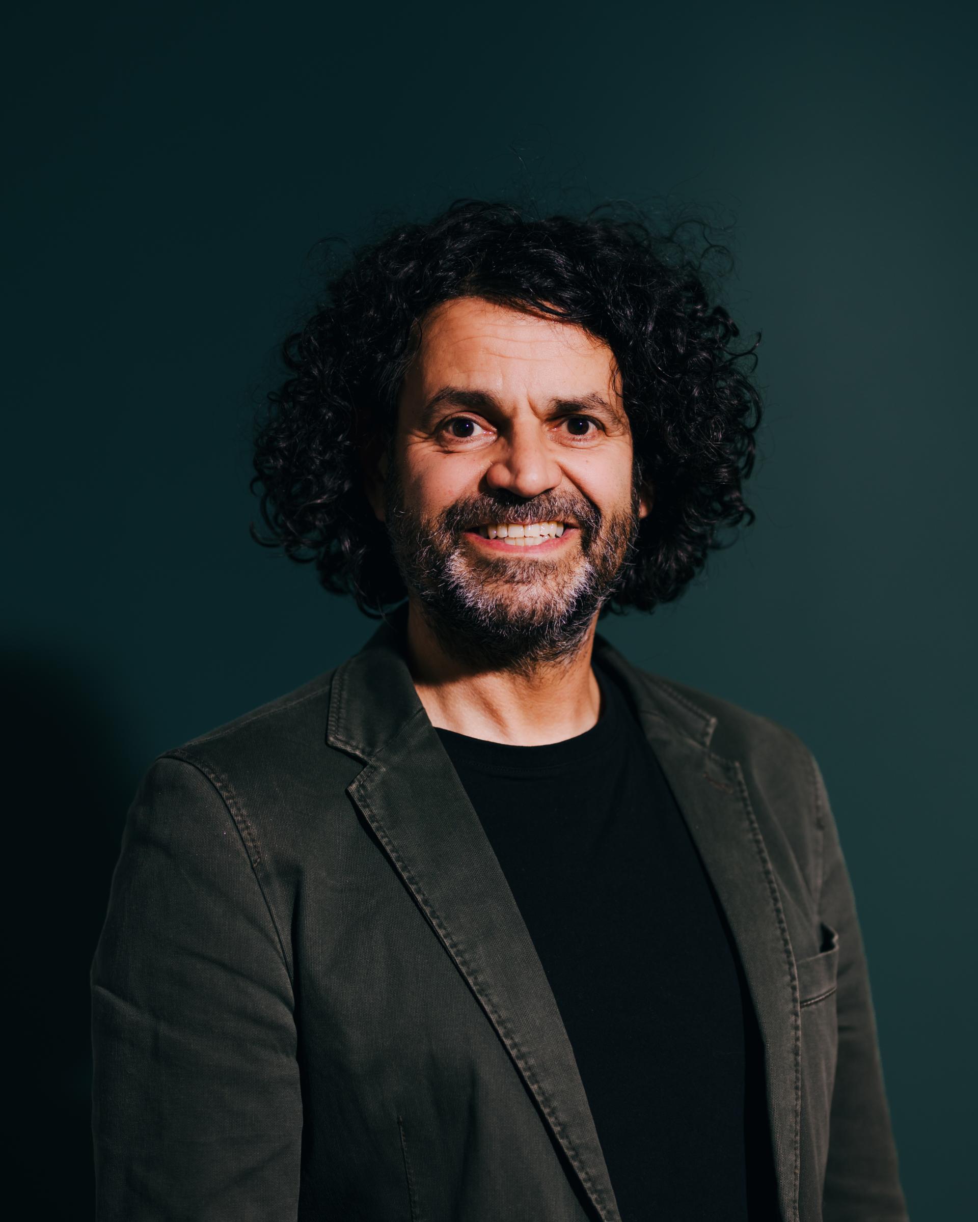 Portrait of a smiling man with curly hair, discussing neurodiversity and flexibility in a creative environment.