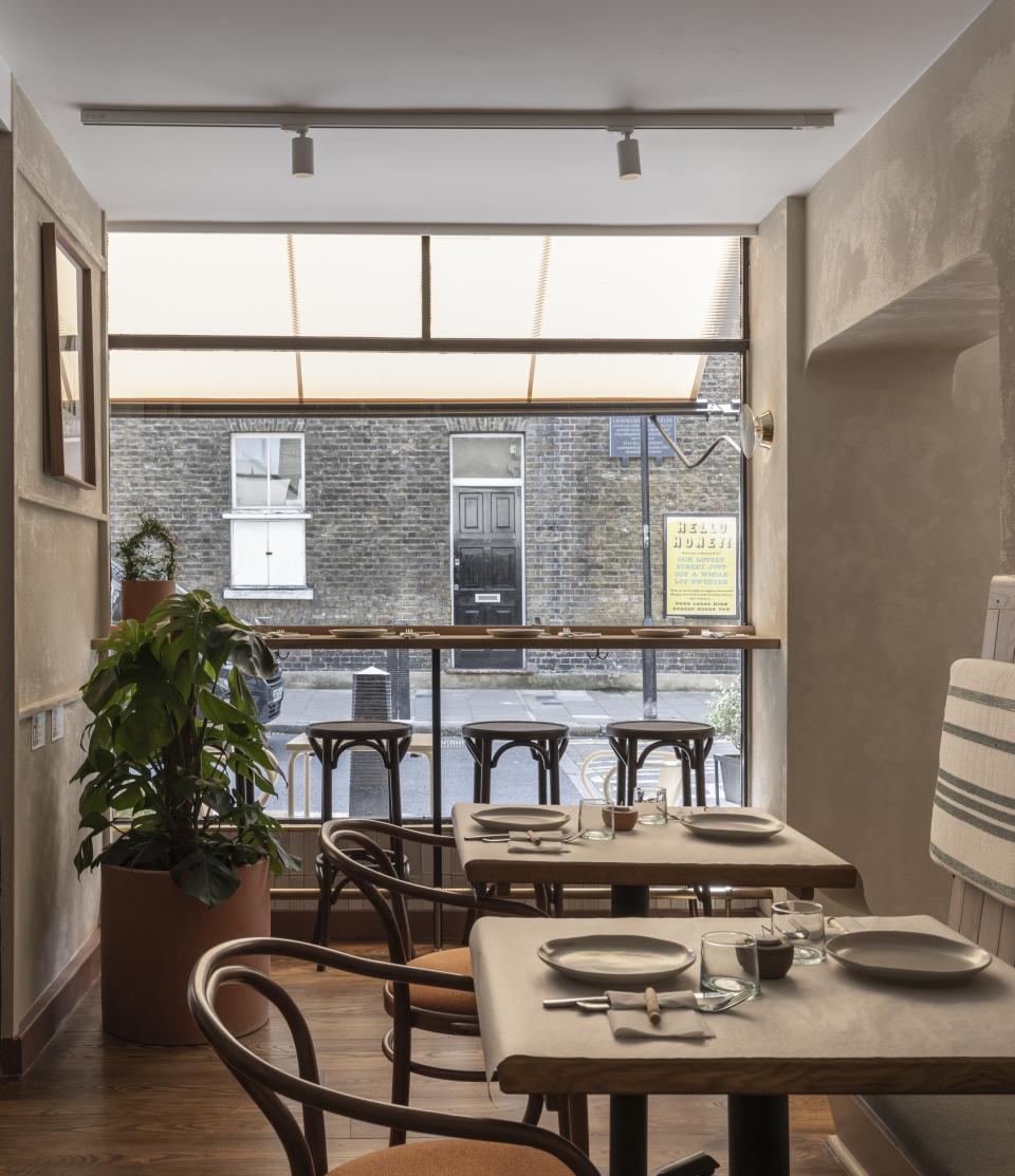 Cozy interior of Honey & Co Bloomsbury featuring wooden tables, chairs, and large window overlooking the street.