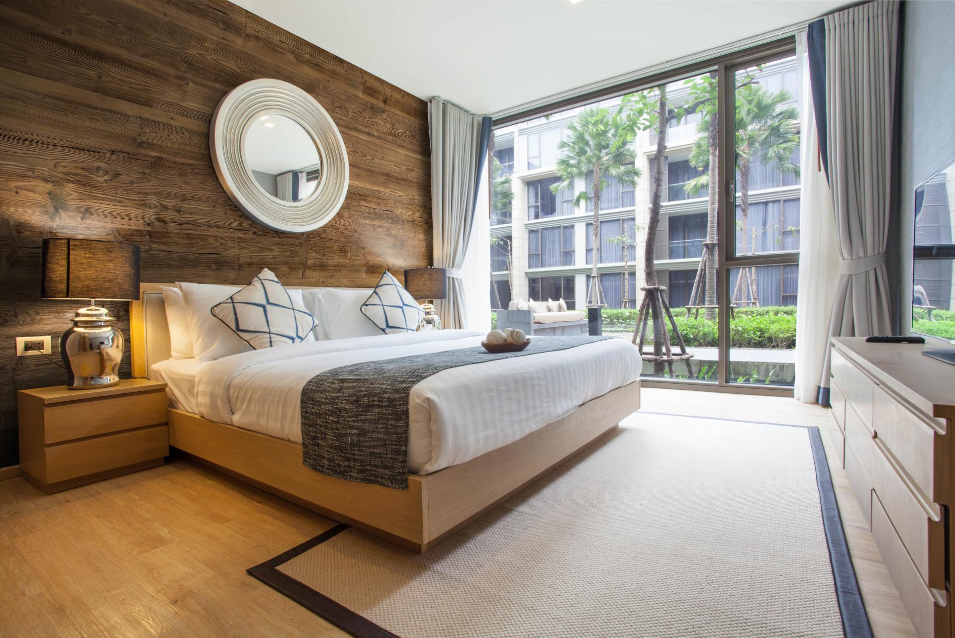Brightly designed modern bedroom featuring wooden accent walls, plush bedding, and large windows with garden views.