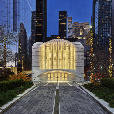 Santiago Calatrava's sculptural church, featuring sleek white curves and illuminated glass, set against a city skyline at dusk.