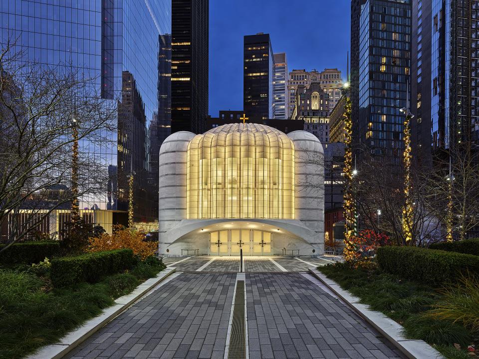 Santiago Calatrava's sculptural church, featuring sleek white curves and illuminated glass, set against a city skyline at dusk.