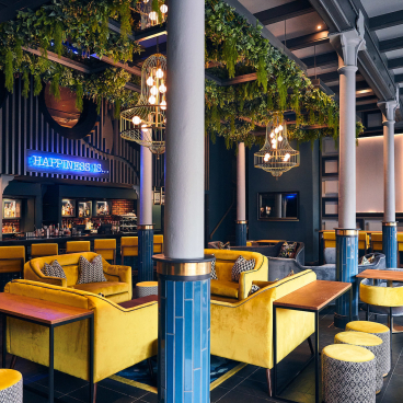 Lively hotel bar featuring luxurious yellow seating, greenery, and stylish decor by Crown Paints for Malmaison & Hotel du Vin.