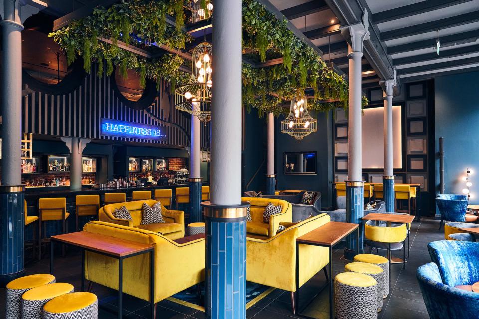 Lively hotel bar featuring luxurious yellow seating, greenery, and stylish decor by Crown Paints for Malmaison & Hotel du Vin.