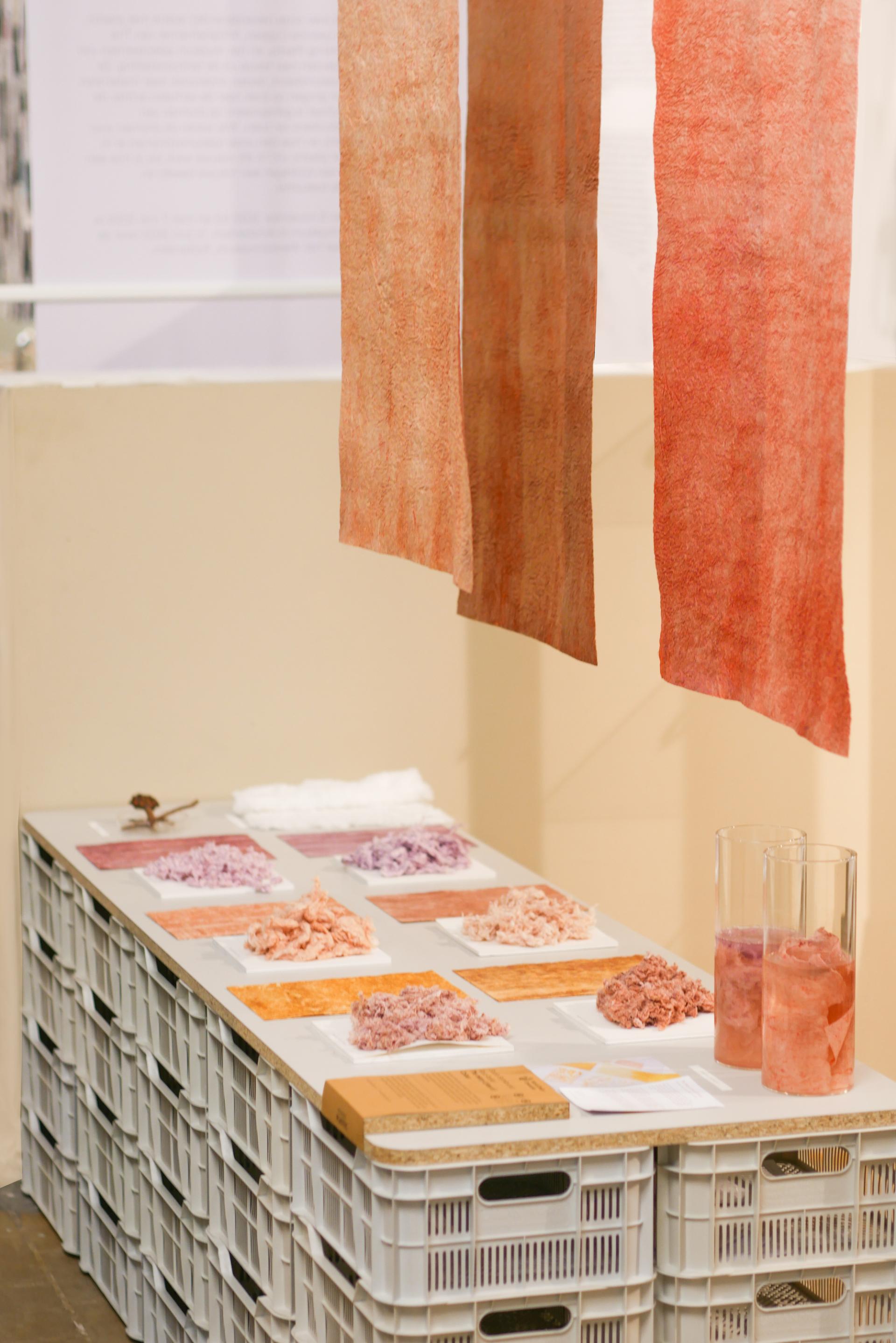 Textiles dyed in earthy tones displayed on a table alongside jars of colored materials, showcasing 2023 design trends.
