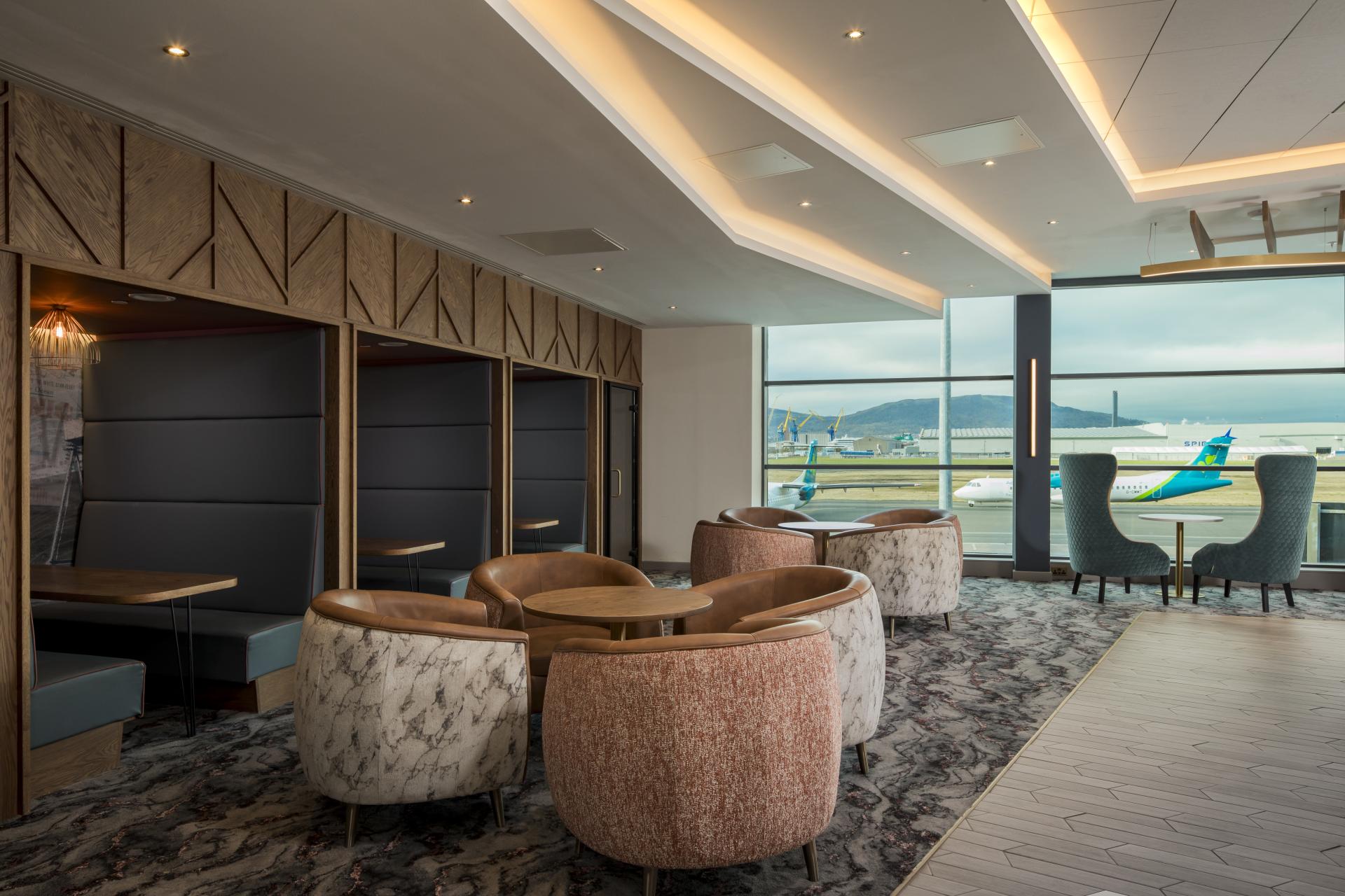 Modern airport lounge interior with stylish seating and a view of aircraft at Manchester Airport.