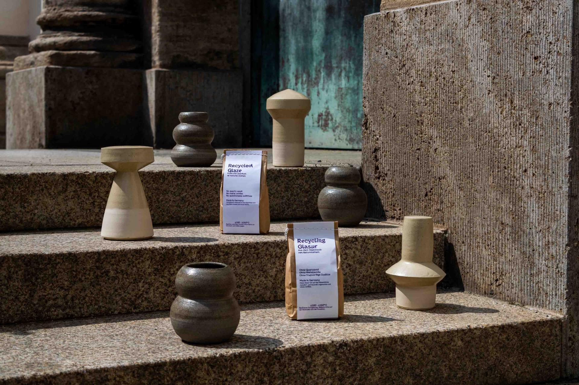 Display of eco-friendly ceramic vases and recycled glaze packaging on stone steps, highlighting sustainable design products.