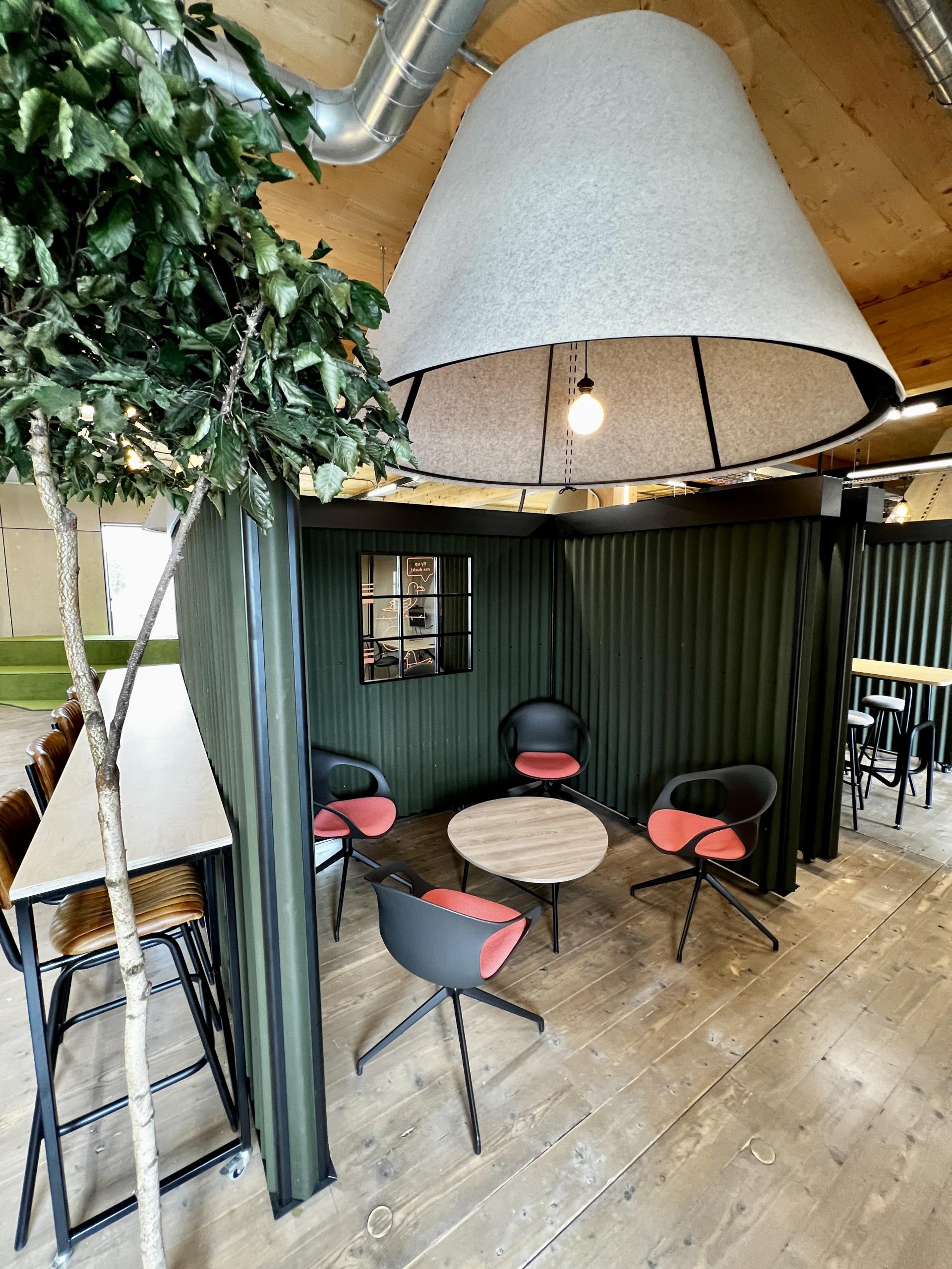 Modern workspace interior featuring eco-friendly design elements, including a large light fixture, seating area, and greenery.