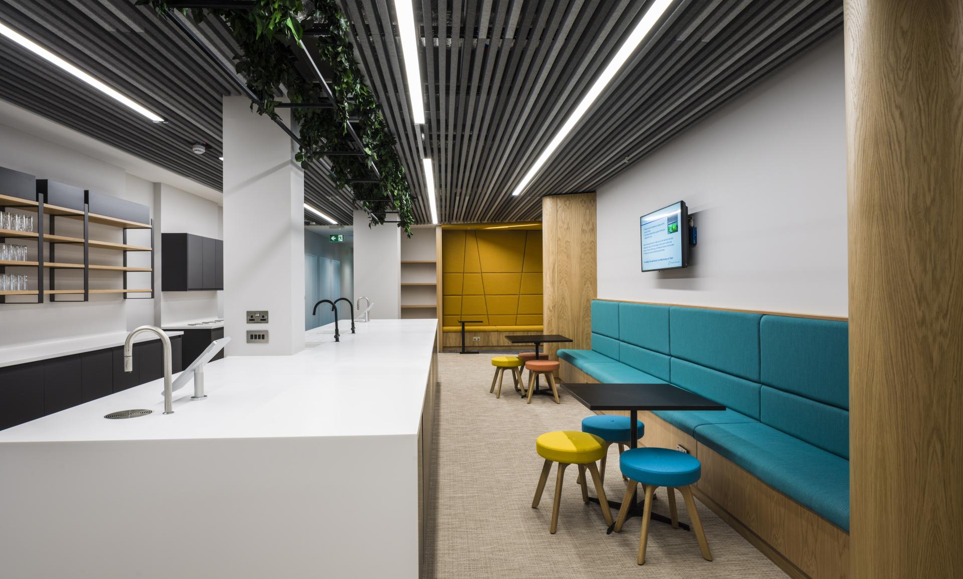 Modern office kitchen area featuring stylish seating, bright colors, and a WELL certified design by Form Design Consultants.