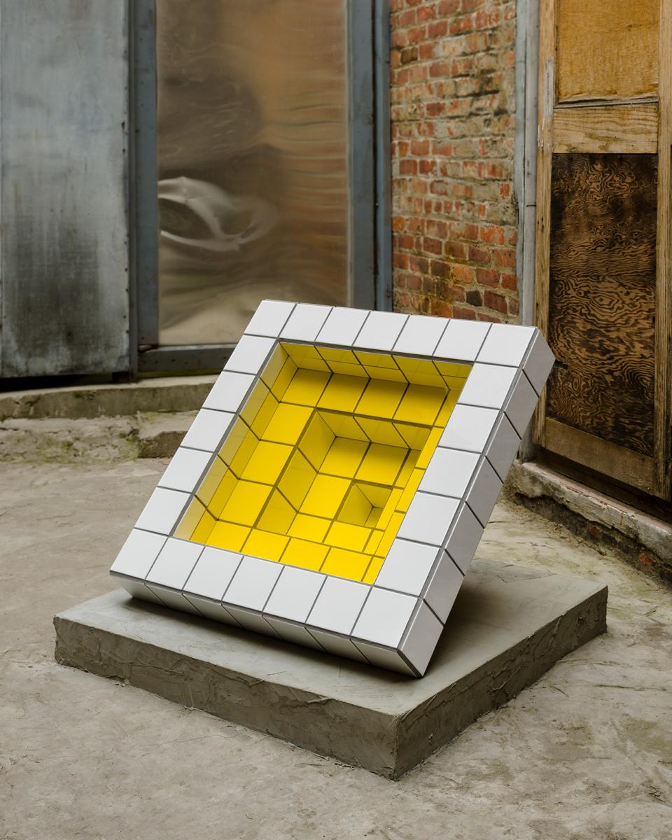 Sculptural artwork by Zac Hacmon, featuring white subway tiles and a vibrant yellow interior, set in an industrial space.