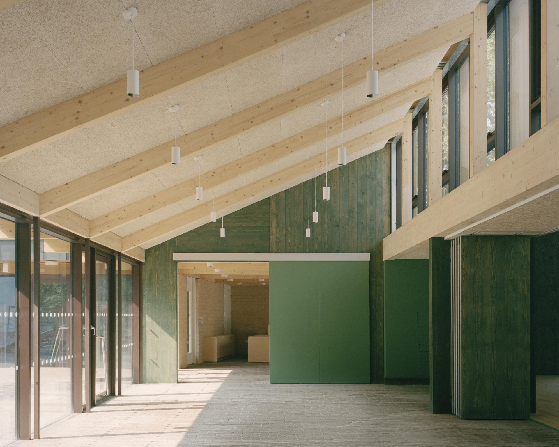 Modern interior showcasing wooden beams, green accent walls, and large windows, highlighting sustainable architecture for RIBA's Stirling Prize.