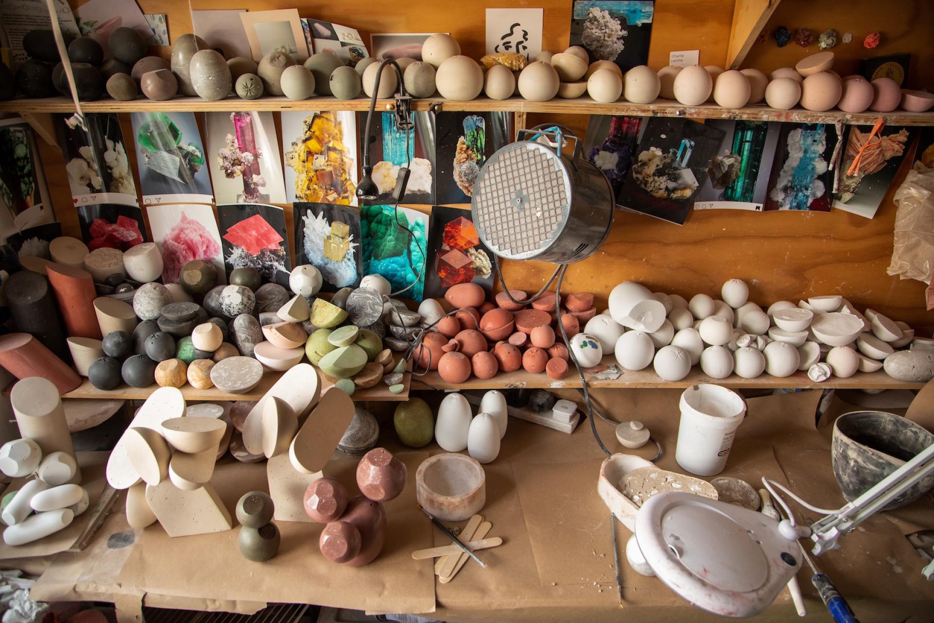 Cluttered workspace of sculptor Vic Wright showcasing various clay sculptures, tools, and inspirational images in her studio.