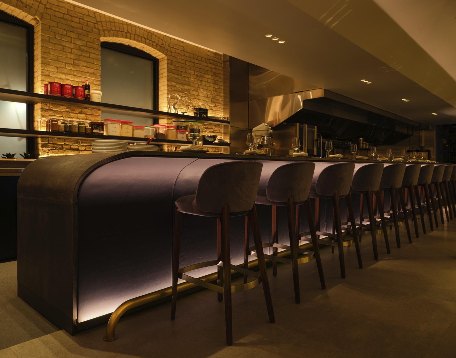 Modern, inviting restaurant interior showcasing a stylish bar with ambient lighting, grey seating, and a sleek design.